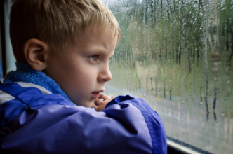 Young boy looking out a window at a rain storm