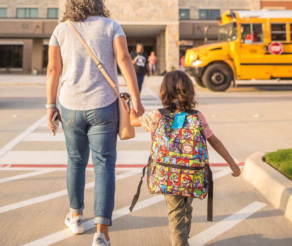 woman and child holding hands walk towards school building