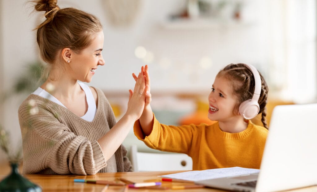 mother giving young young daughter a high-five during online lesson